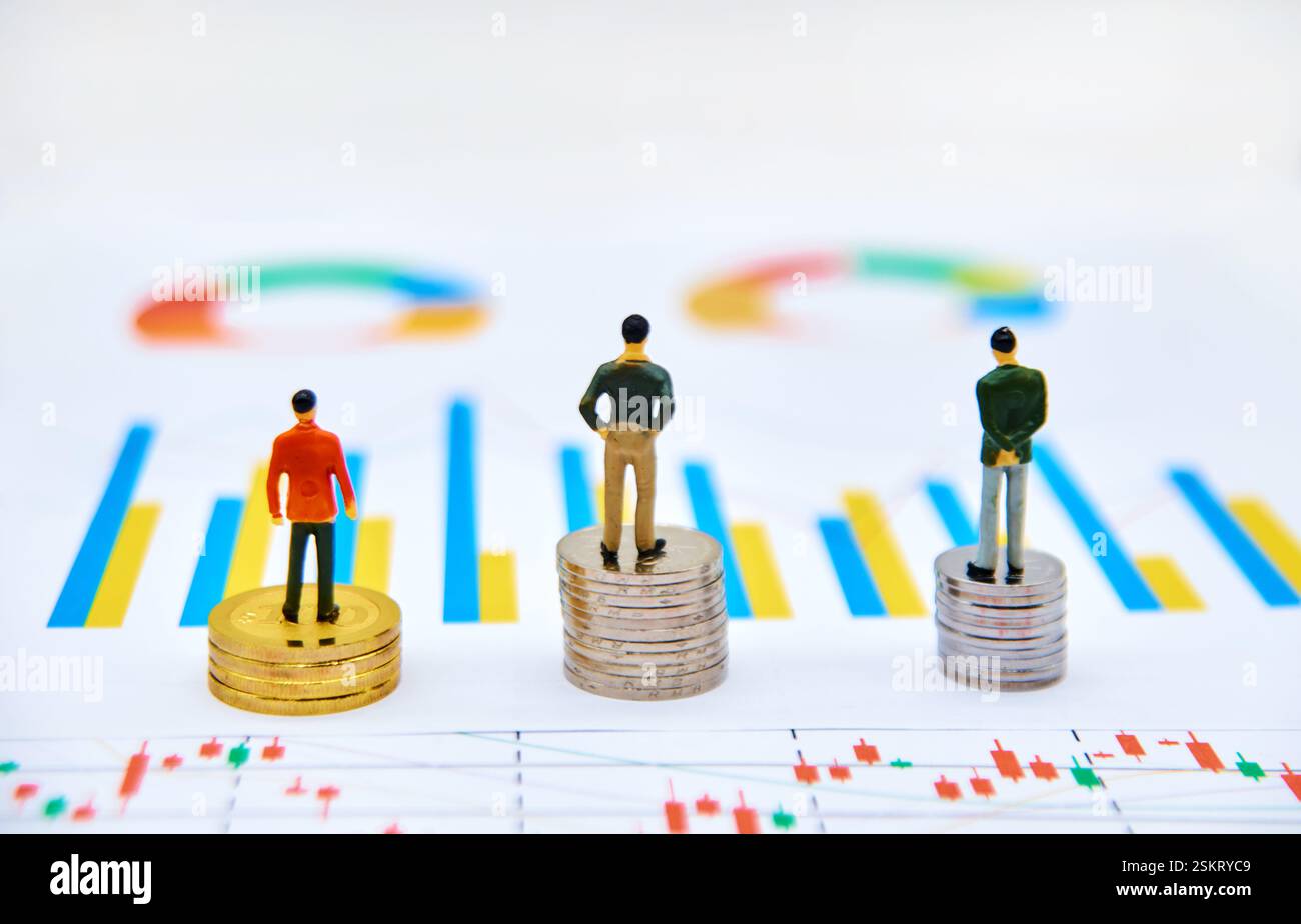 Tre figure in miniatura che si trovano su una pila di monete e osservano i dati Foto Stock