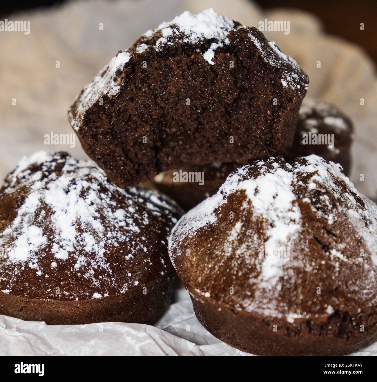 Primo piano di un muffin al cioccolato morso con sopra zucchero a velo, posto su carta pergamena. Foto Stock