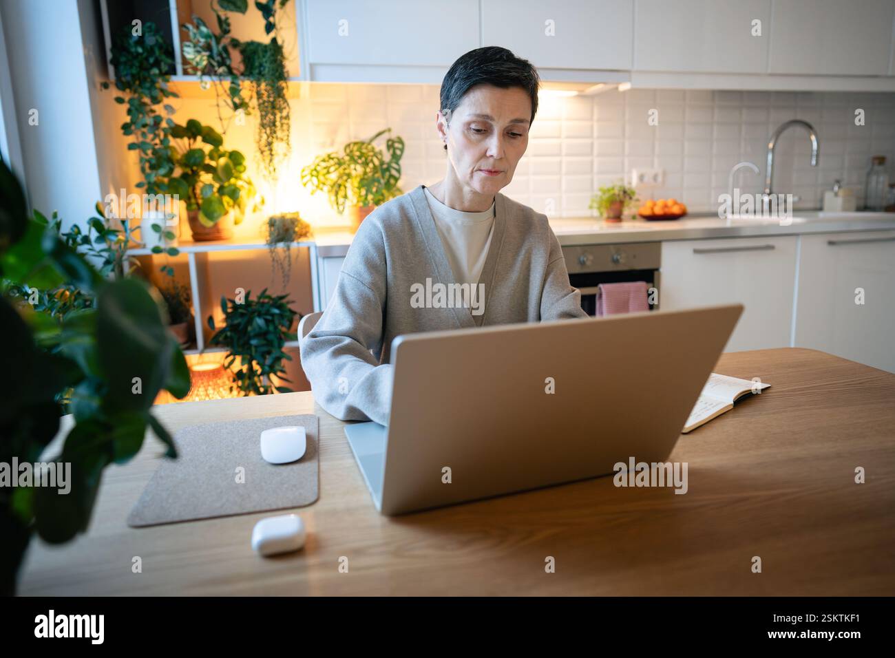 Donna premurosa e stanca che lavora a un progetto con un notebook in cucina a casa, che deve affrontare delle scadenze Foto Stock