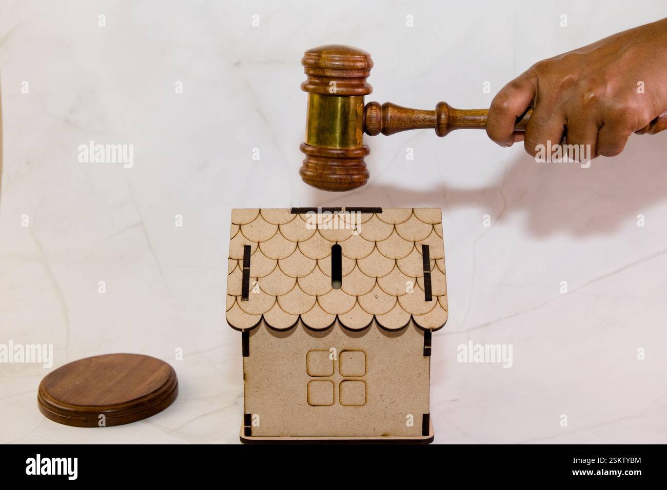 Una mano regge un martelletto di legno sopra un piccolo modello di casa in legno, simboleggiando un processo di asta immobiliare. Foto Stock