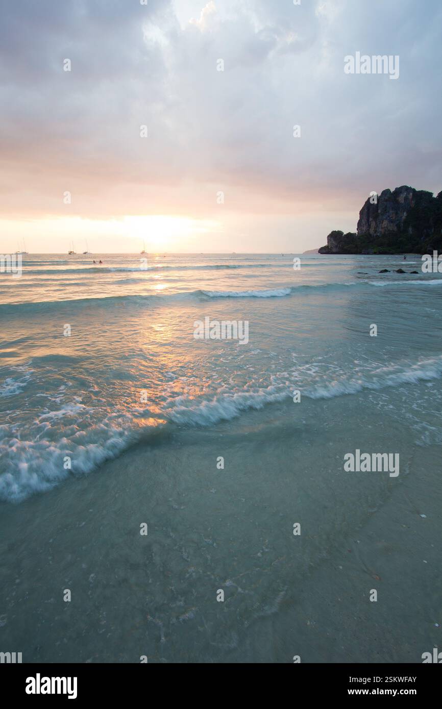 Un tranquillo tramonto a Railay Beach, Thailandia, con dolci onde che si infrangono sulla spiaggia sabbiosa. Foto Stock