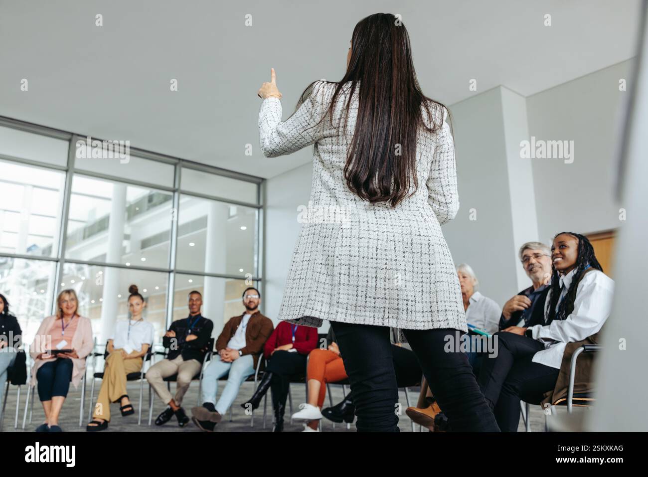 Relatrice femminile che conduce un seminario motivazionale con un gruppo diversificato di partecipanti in una moderna sala conferenze. Concetto di leadership e discorso pubblico Foto Stock