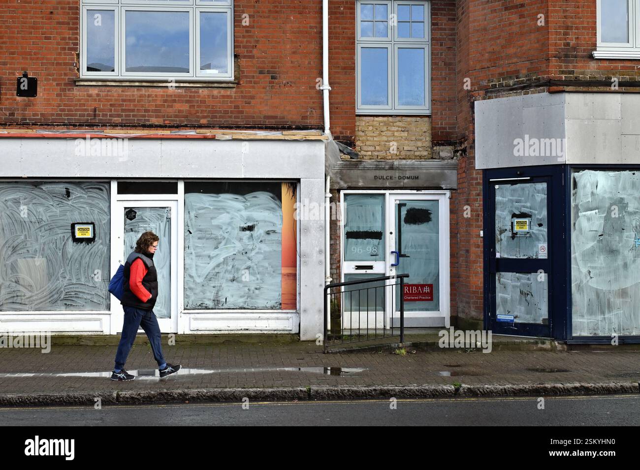 Una donna pedonale che passa davanti a negozi chiusi in una città urbana, Shepperton Surrey Inghilterra, Regno Unito Foto Stock