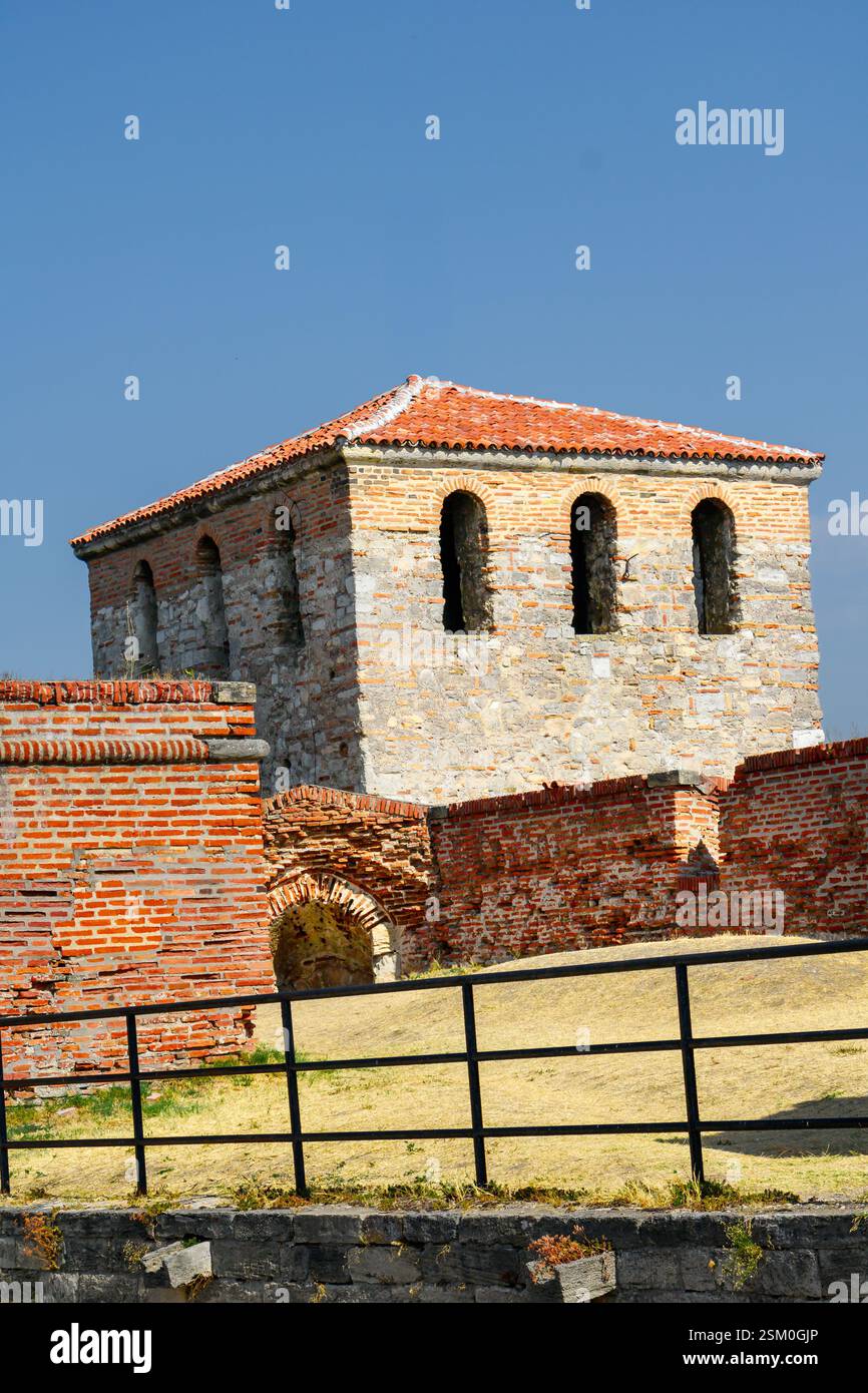 Una struttura in pietra ben conservata con finestre ad arco sorge tra i resti di antiche mura sotto un cielo azzurro. La posizione suggerisce una storia Foto Stock