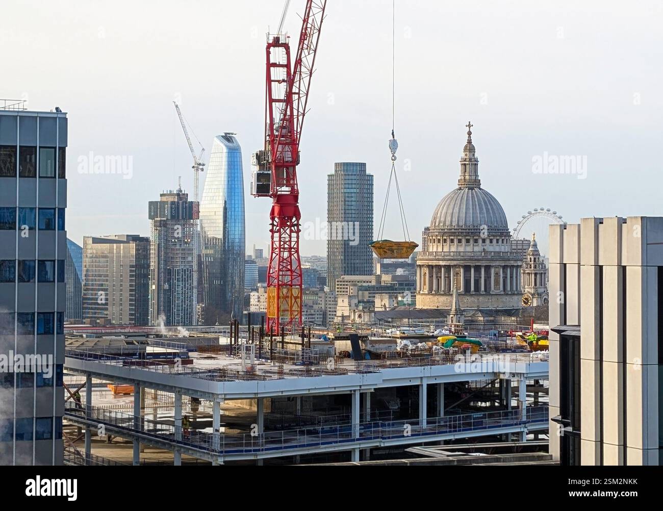 29 gennaio 2025 Londra, Regno Unito - Un dinamico paesaggio urbano caratterizzato da un cantiere in primo piano con una struttura parzialmente costruita e un grande cr rosso Foto Stock