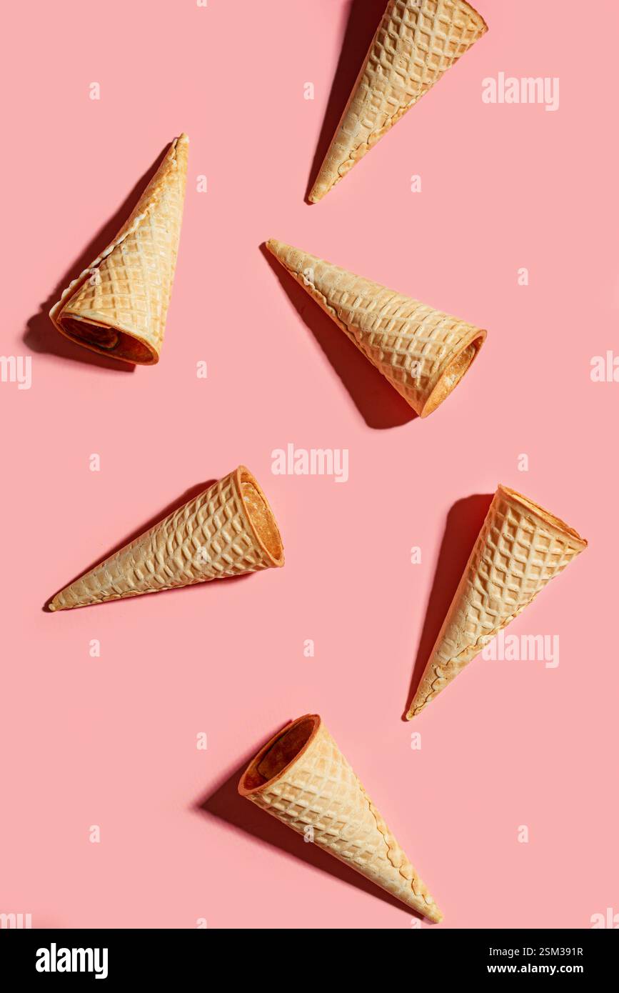 Disposizione creativa dei coni per cialde di gelato su sfondo rosa pastello, vista dall'alto. Concetto di dessert dolce estivo. Foto Stock