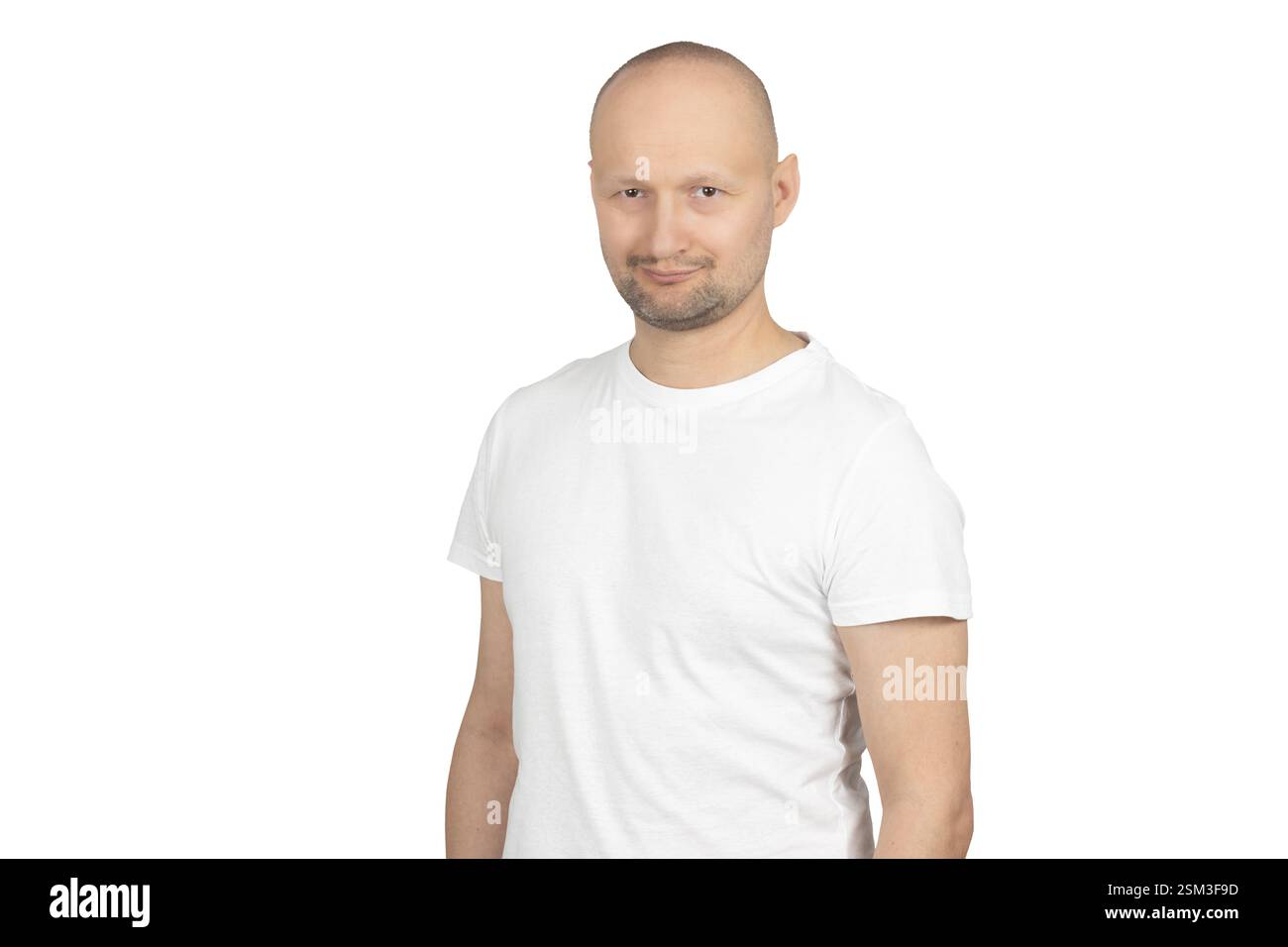 Un uomo caucasico calvo con la barba corta indossa una t-shirt bianca e dà un sorriso sottile e affascinante mentre guarda direttamente la fotocamera. Foto Stock
