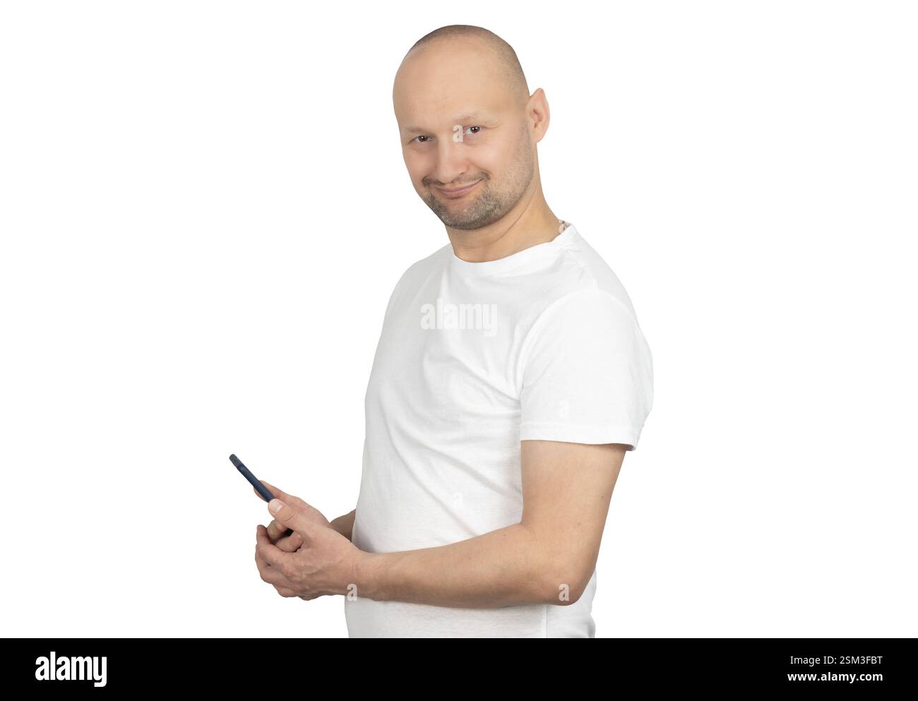 Un uomo caucasico calvo con una barba corta è in posa rilassata, tenendo in mano uno smartphone e sorridendo con sicurezza. Foto Stock
