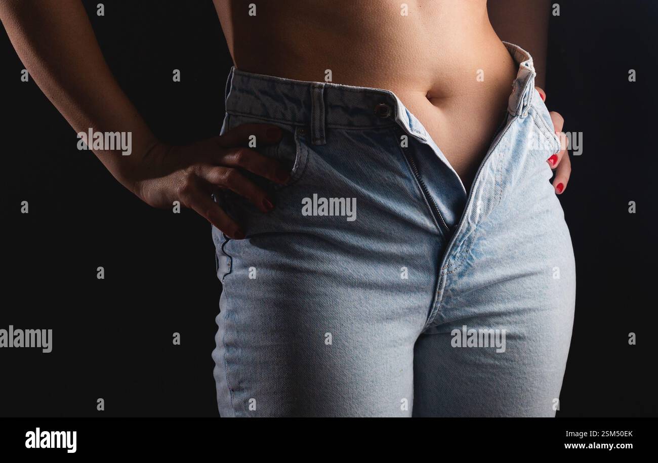 Donna sovrappeso in jeans stretti su sfondo nero. Concetto di peso eccessivo Foto Stock