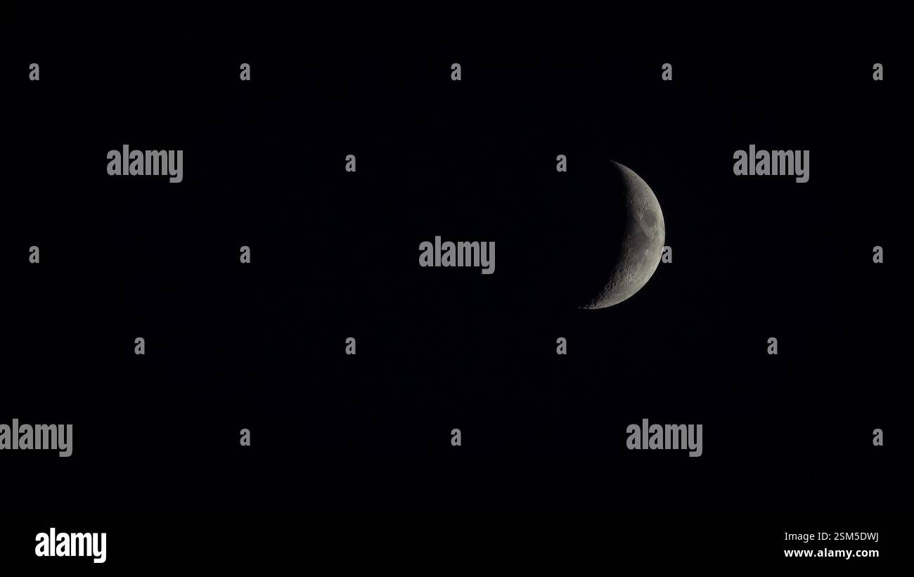 Una luna crescente ondeggiante si illumina contro un cielo notturno nero, rivelando intricati dettagli superficiali e crateri in questa sorprendente immagine di astrofotografia lunare. Foto Stock