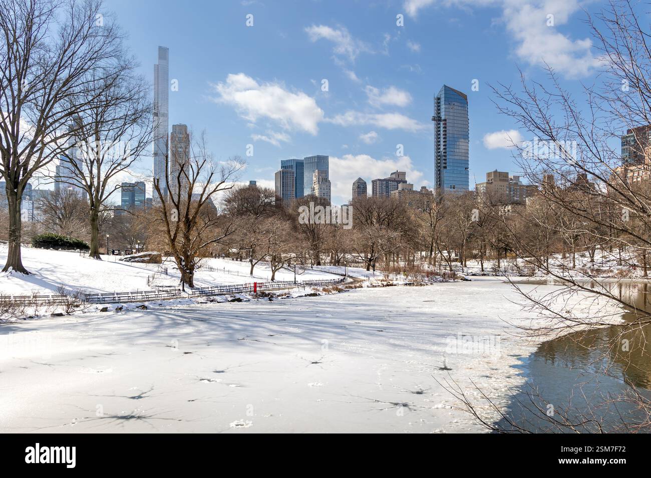 Central Park dispone di un tranquillo lago ghiacciato circondato da un terreno innevato. Lo skyline di Manhattan si erge alto sullo sfondo in un giorno d'inverno. Foto Stock