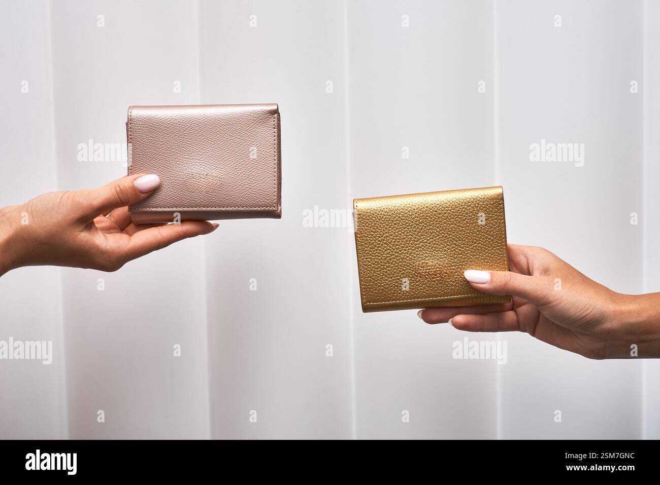 Mani con eleganti portafogli in oro rosa e metallizzato su sfondo bianco, che mettono in risalto lo stile minimalista, gli accessori e il concetto di moda Foto Stock