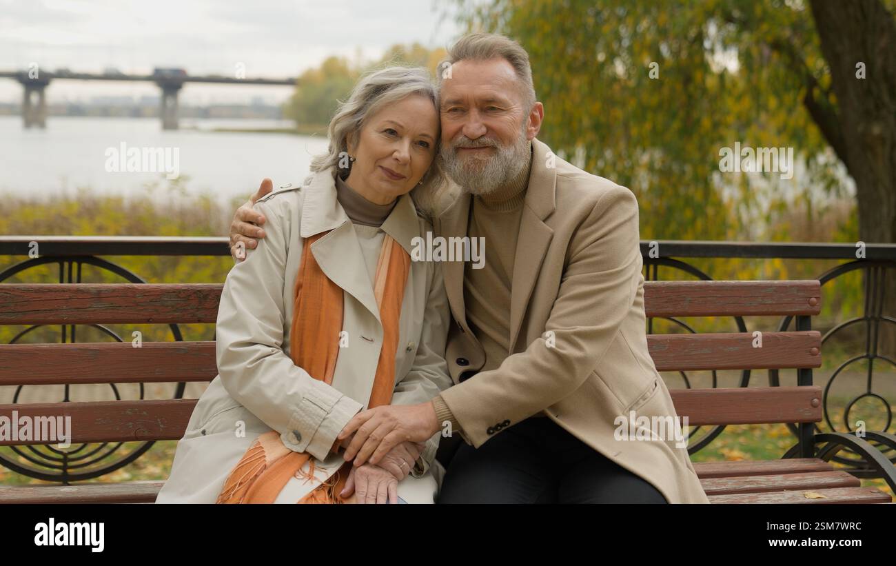 Pensionato anziana donna caucasica uomo legando affettuosa coppia d'amore maschio femmina abbracciando sulla panchina in parco città felice famiglia di mezza età 60 anni Foto Stock