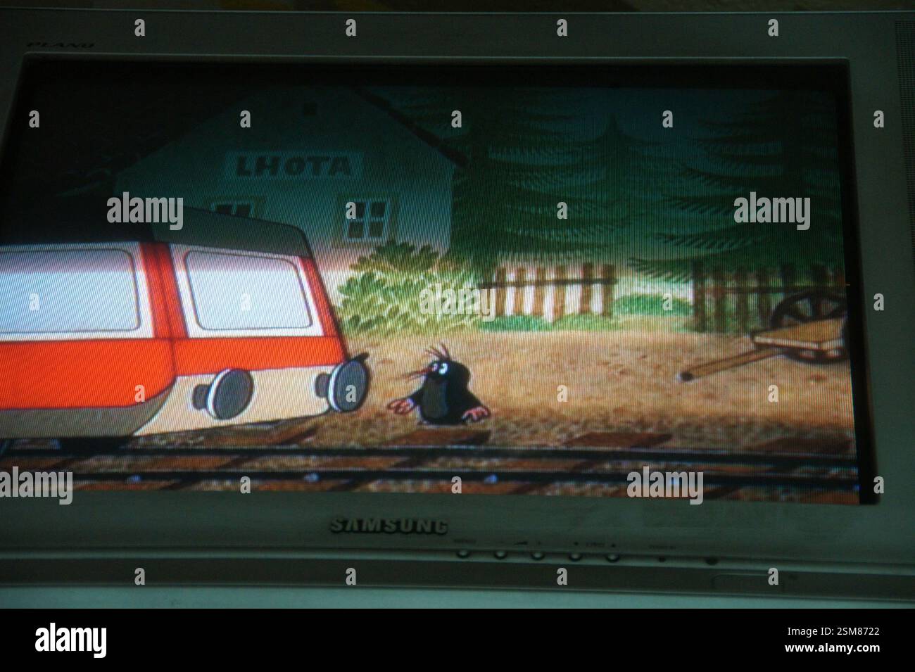 La piccola Mola, un popolare personaggio dei cartoni animati per bambini, è vista accanto a un treno rosso e bianco su un binario ferroviario. Lussureggianti alberi verdi e una casa pittoresca Foto Stock