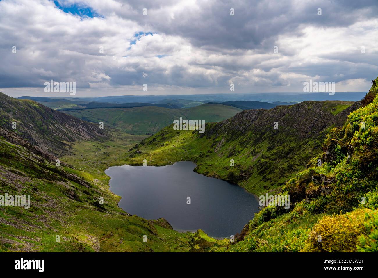 Vista aerea mozzafiato di Llyn Cau incastonata tra le cime scoscese di Cadair Idris sotto i suggestivi cieli Cloud-Laden Foto Stock