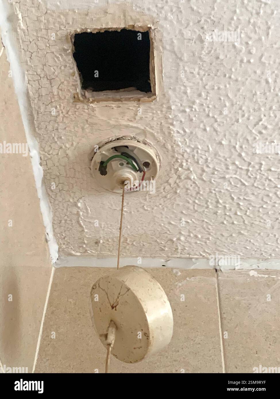 Illuminazione interna su un soffitto guasto dei fili elettrici inglesi del Regno Unito guasto del cavo flessibile del filo del filo rosa guasto del materasso bianco del tetto - Immagine stock catturata con smartphone