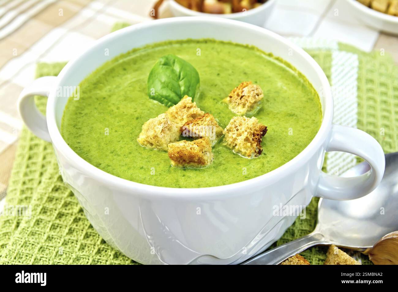 Zuppa verde purea in una ciotola bianco con crostini e foglie di spinaci su un tovagliolo sul tessuto di sfondo Foto Stock