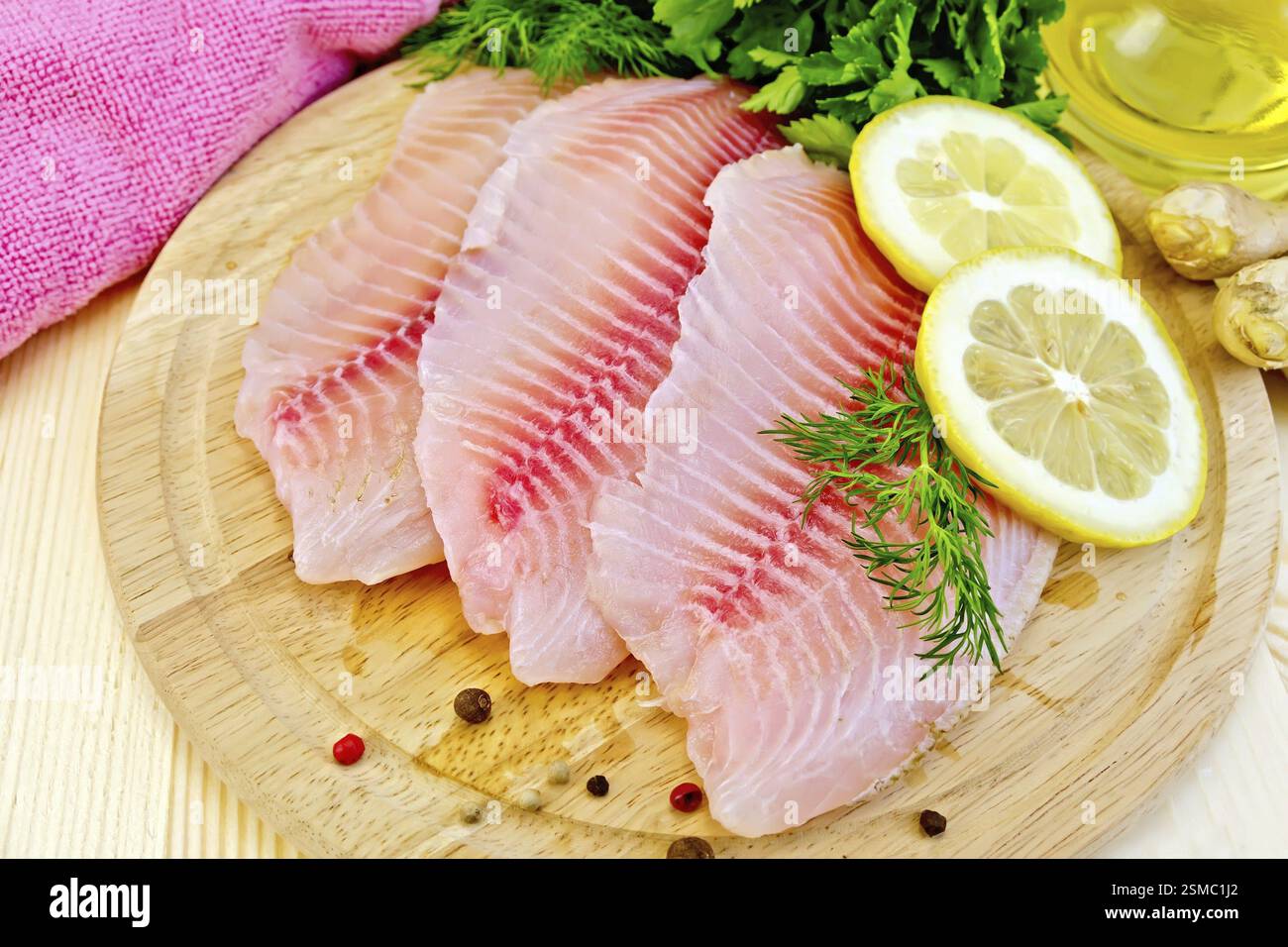 Filetti di tilapia con aneto, limone, zenzero, stoffa, olio vegetale in un decanter su sfondo di pannelli di legno Foto Stock