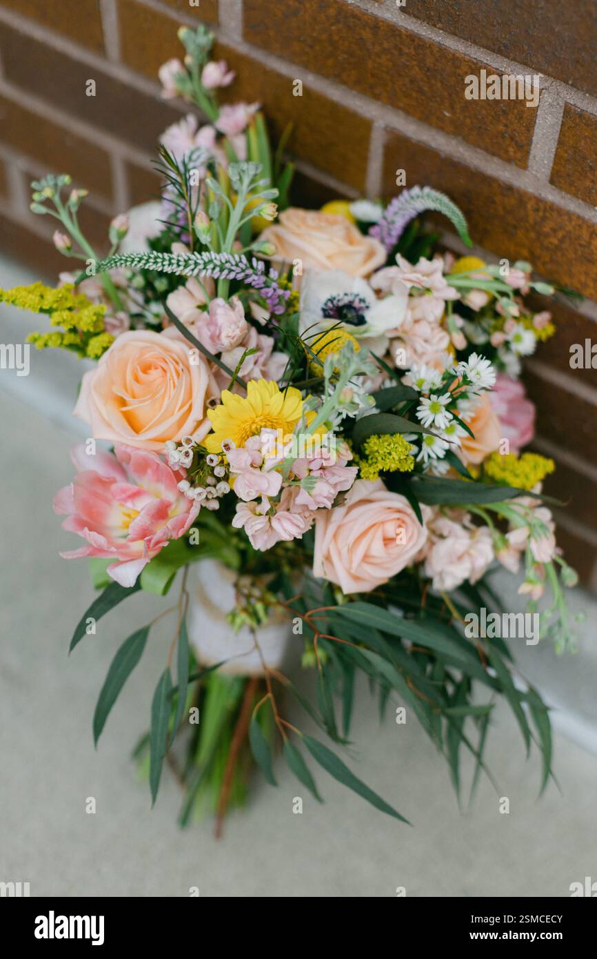 Delicati fiori di rosa, giallo e bianco riempiono il bouquet posto vicino a una parete rustica di mattoni. Foto Stock