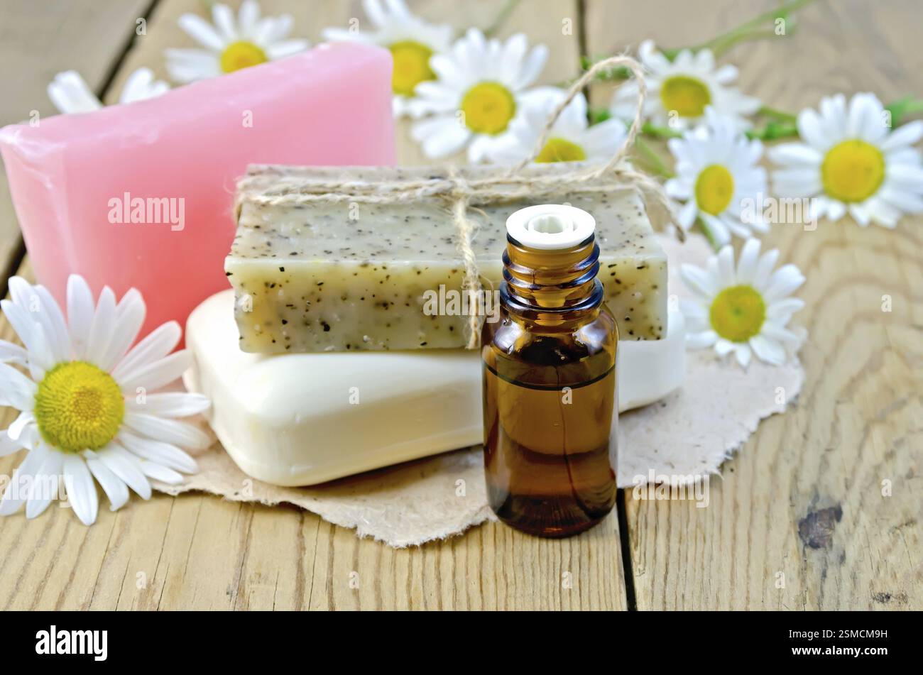 L'olio in una bottiglia, Sapone casalingo su un pezzo di carta, daisy fiori su uno sfondo di tavole di legno Foto Stock