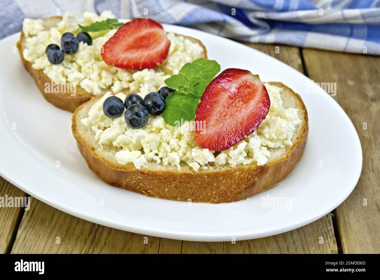 Fette di pane con crema di ricotta, menta, mirtilli e fragole su una piastra su un tavole di legno sfondo Foto Stock