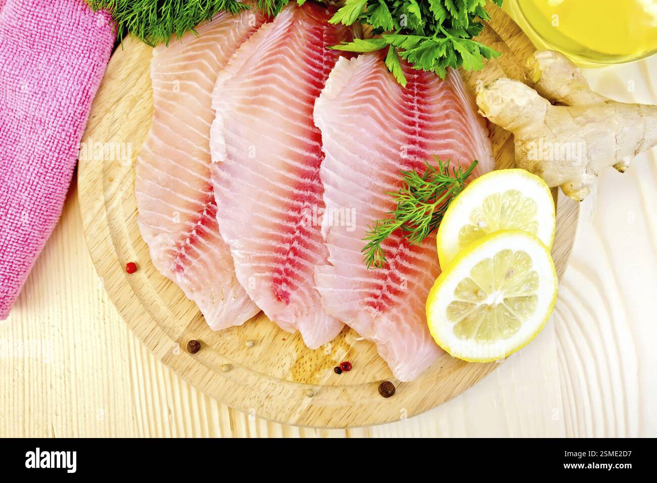 Filetti di tilapia con aneto, limone, zenzero, stoffa, olio vegetale su fondo di legno Foto Stock