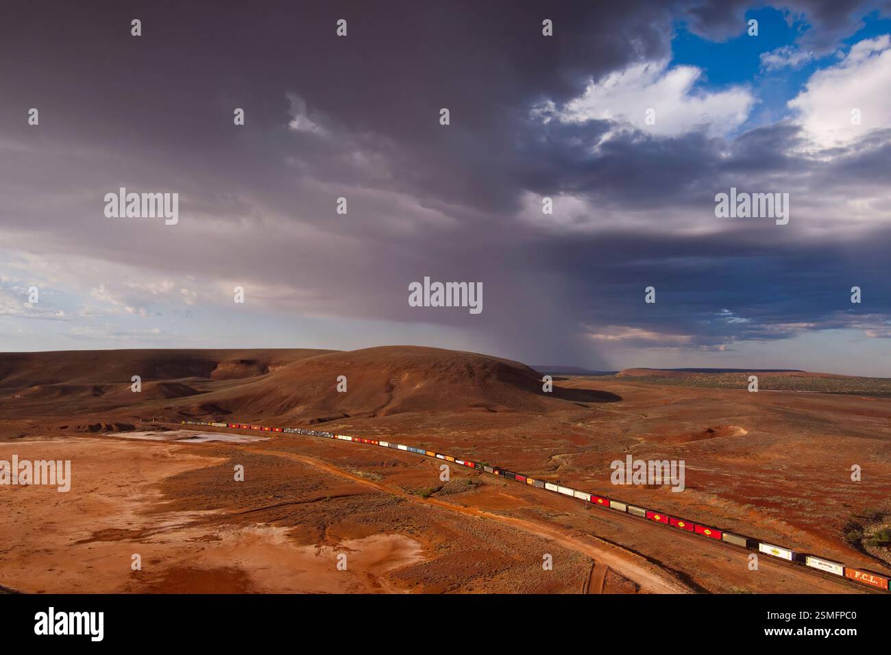 Aereo di un treno intermodale per container a doppio strato che attraversa un vasto e arido paesaggio con colline ondulate e vegetazione sparsa. Foto Stock