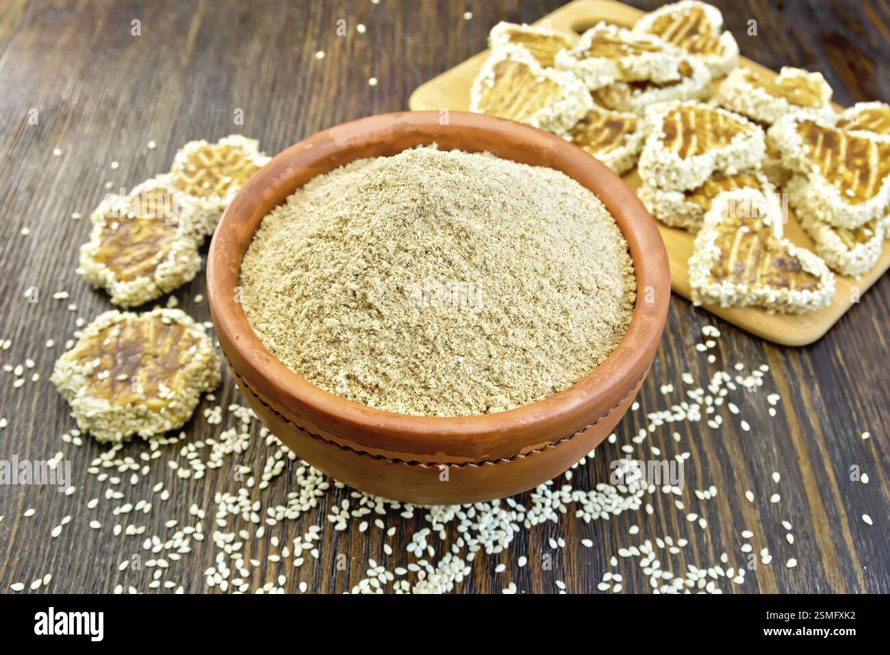 Il SESAMO la farina in una ciotola di argilla e biscotti fatti in casa su tavole di legno sfondo Foto Stock