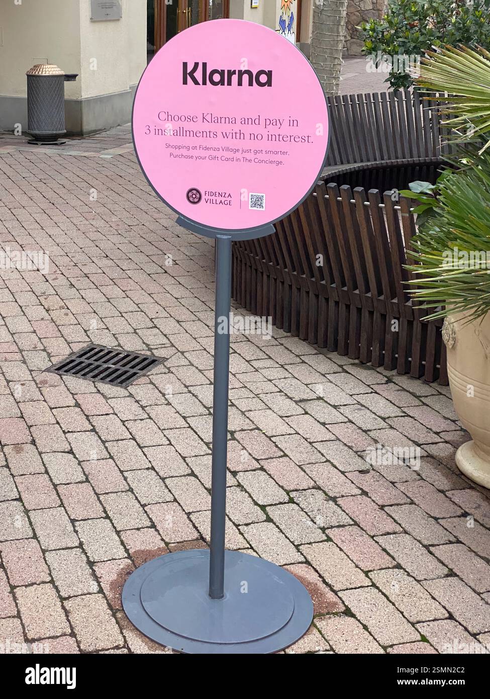 Insegna rosa Klarna che offre il pagamento in tre rate senza interessi, collocata all'esterno del centro commerciale outlet di lusso Fidenza Village in Italia Foto Stock