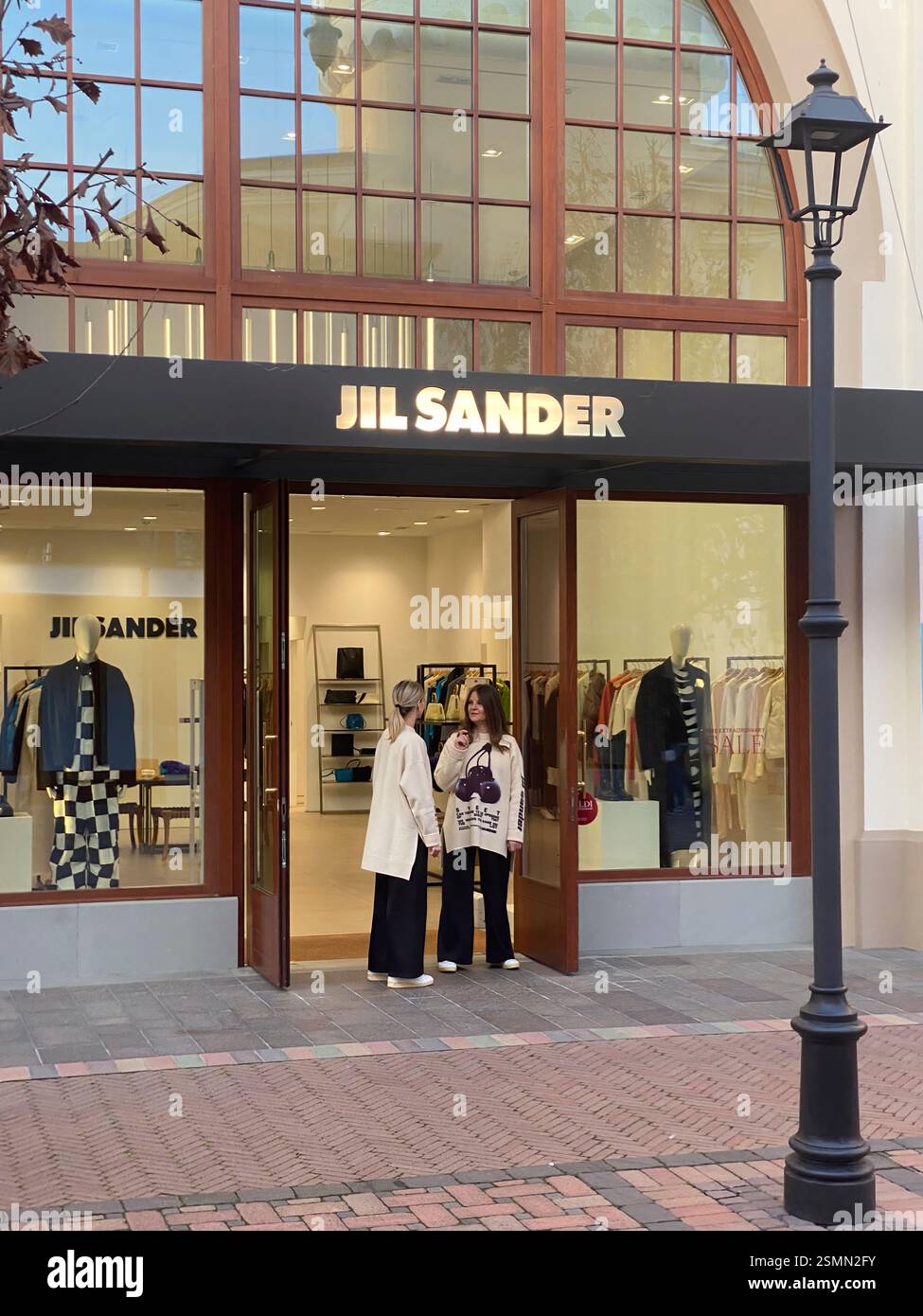 Due donne che chiacchierano all'ingresso del negozio Jil Sander del centro commerciale outlet di lusso Fidenza Village in Italia Foto Stock