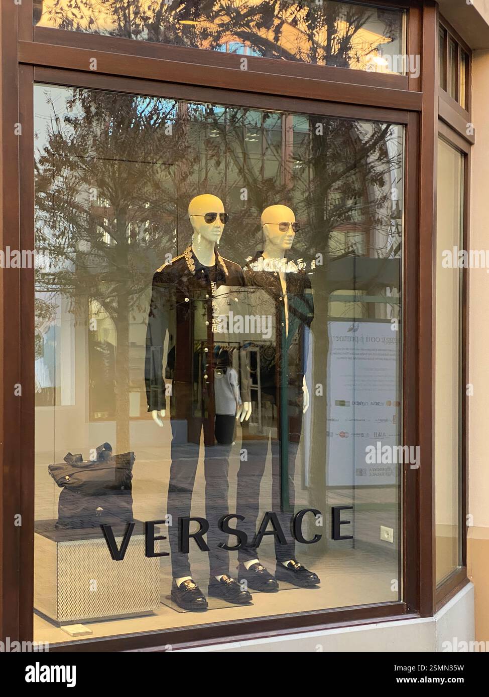I manichini che indossano abbigliamento e accessori Versace sono esposti in una vetrina del Fidenza Village, un centro commerciale outlet di lusso in Italia Foto Stock
