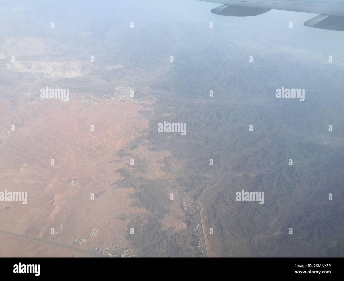 Il vasto deserto di Dubai si dispiega sotto l'ala dell'aeroplano, inondato dalla calda luce del sole. Le dune di sabbia rotolano maestosamente verso l'orizzonte, un paesaggio aspro Foto Stock