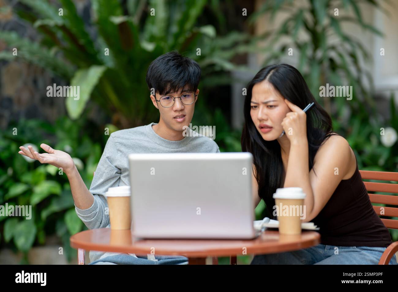 Due asiatici stressati e frustrati sono seduti di fronte a un notebook, lottando con il loro progetto, affrontando un problema durante una riunione informale Foto Stock