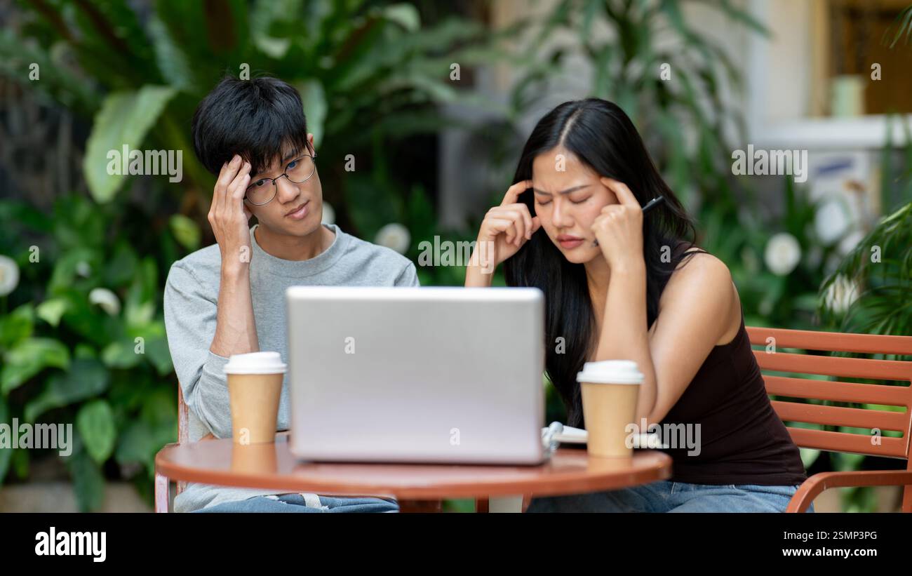Due asiatici stressati e frustrati sono seduti di fronte a un notebook, lottando con il loro progetto, affrontando un problema durante una riunione informale Foto Stock