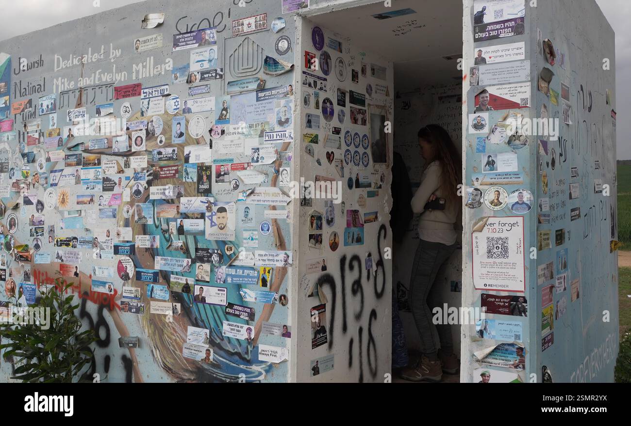 Le persone visitano il "Bunker of Death" fuori Kibbutz Re'im con adesivi commemorativi che commemorano i soldati IDF uccisi nella guerra israeliana a Gaza e ter­ror vic­tims dopo l'attacco di Octo­ber 7 da parte di Hamas, l'11 febbraio 2025 a Re'im, Israele. "Bunker of Death" è un termine usato per indicare il rifugio antiatomico indipendente chiamato in ebraico "Migunit" situato a Re'im Junction e Alumim Junction, dove decine di giovani israeliani furono uccisi e presi in ostaggio mentre fuggivano dal massacro del festival musicale Re'im il 7 ottobre 2023. Foto Stock