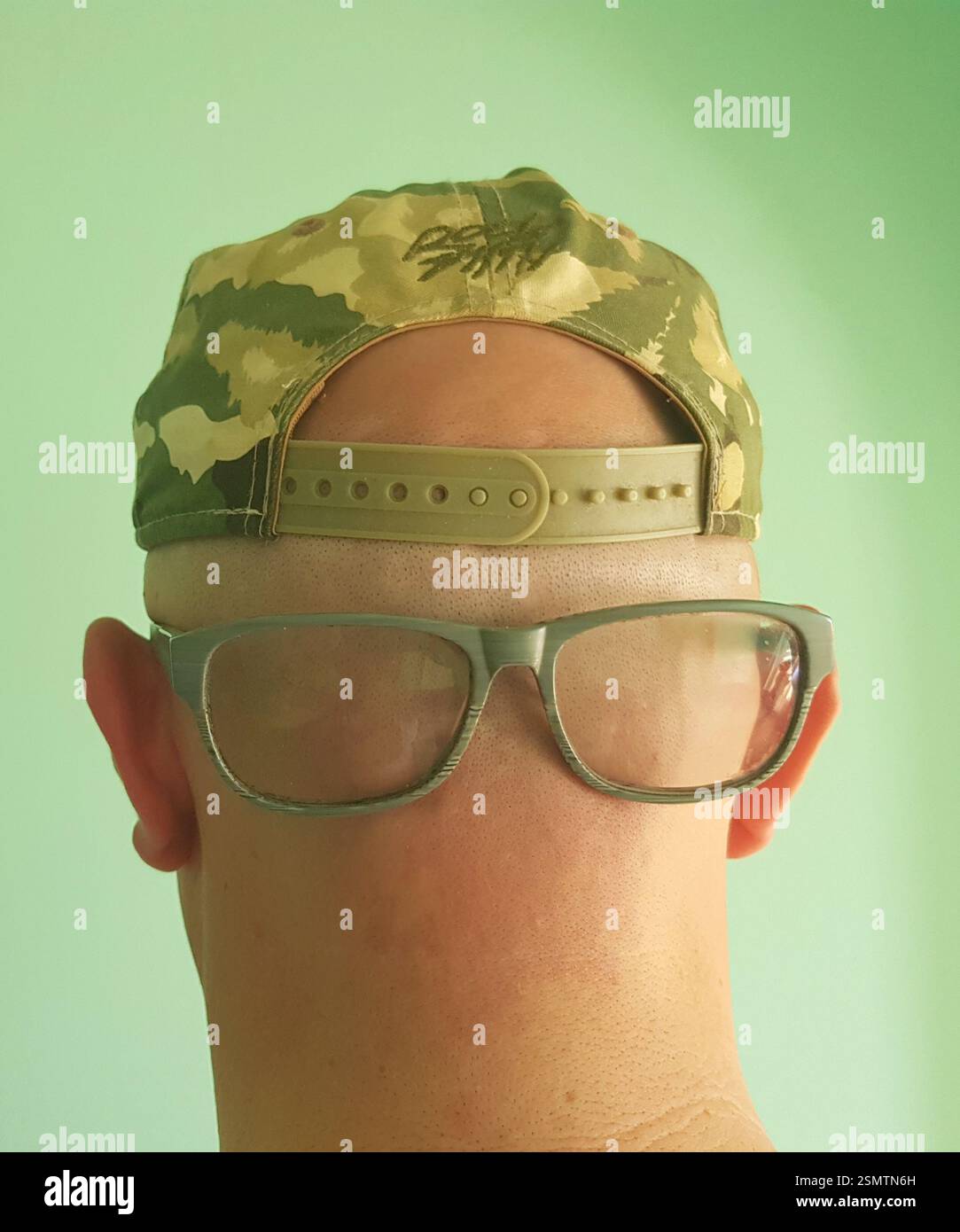 Pensieri silenziosi – testa rasata e Snapback contro il muro verde Foto Stock