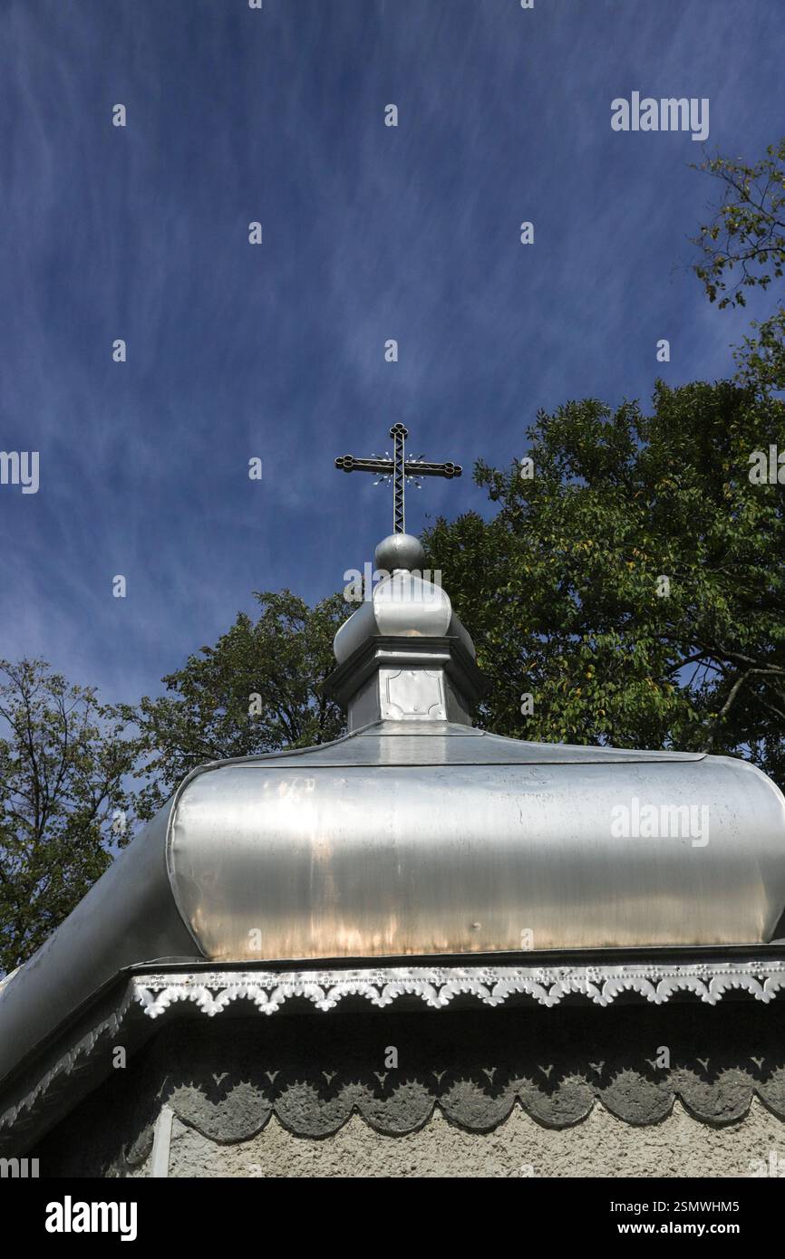Una cupola argentata sormontata da una croce si estende verso il cielo, circondata da lussureggianti alberi verdi sotto un cielo azzurro e limpido a mezzogiorno. Foto Stock
