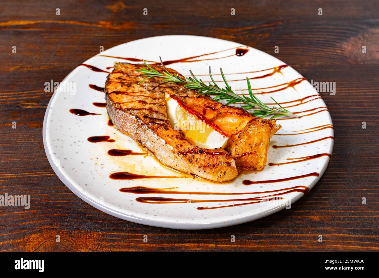 Filetto di pesce alla griglia ben presentato guarnito con erbe fresche e limone, con riduzione balsamica. Servito su un piatto bianco Foto Stock