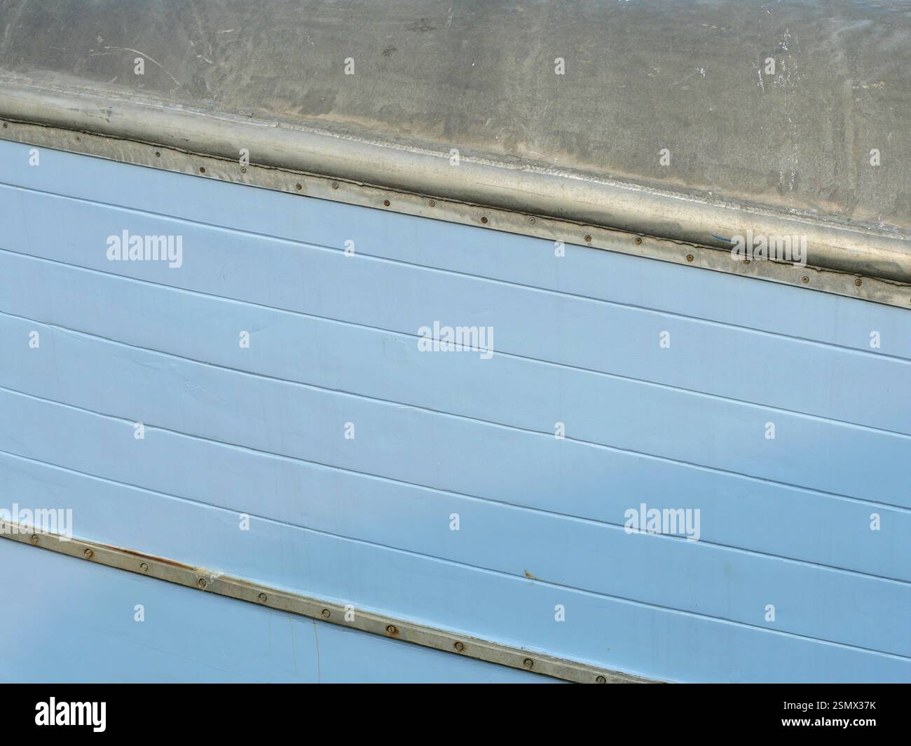 La parete blu chiaro di una barca da pesca con acciaio zincato e rivettato e ringhiere ha un aspetto marittimo e robusto. Foto Stock