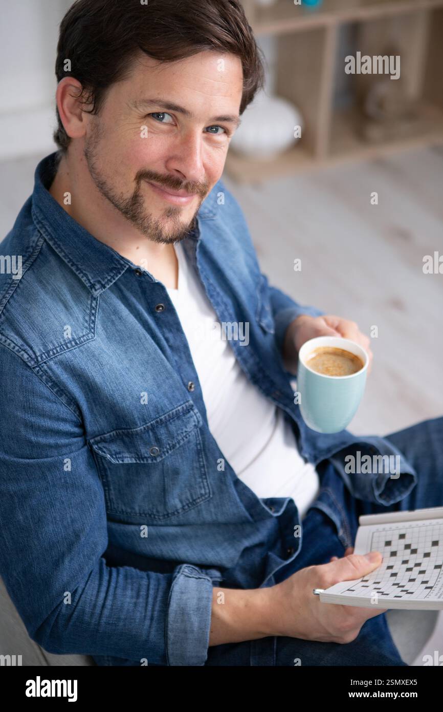 uomo felice che beve caffè e fa parole incrociate Foto Stock