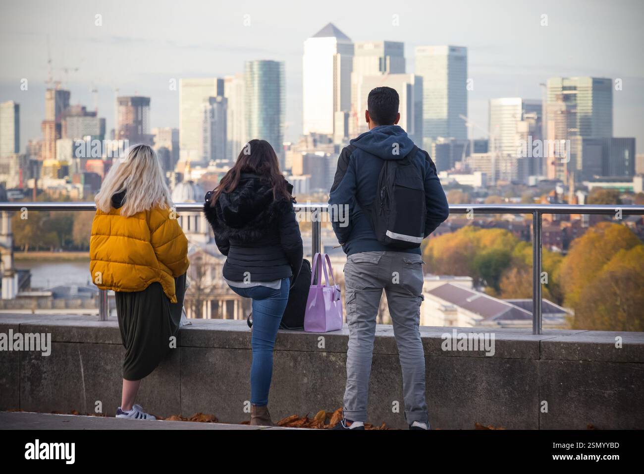 Amici che si trovano a Greenwich Hill con il paesaggio urbano di Canary Wharf sullo sfondo a Londra, Regno Unito Foto Stock