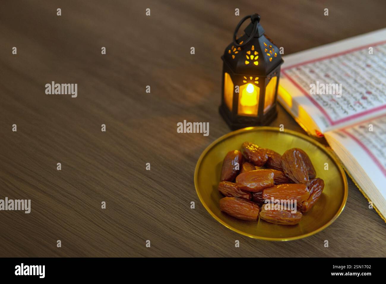 Una ciotola di datteri, una lanterna illuminata e un al Corano aperto su una tavola di legno, simboleggiando il mese sacro islamico del Ramadan. Copia spazio per il testo. Foto Stock