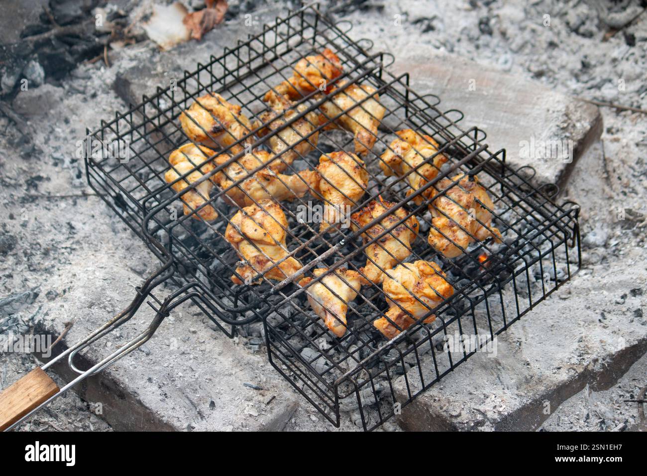 Ali di pollo fritte sopra un fuoco su una griglia di metallo. Concetto di cibo da campeggio Foto Stock