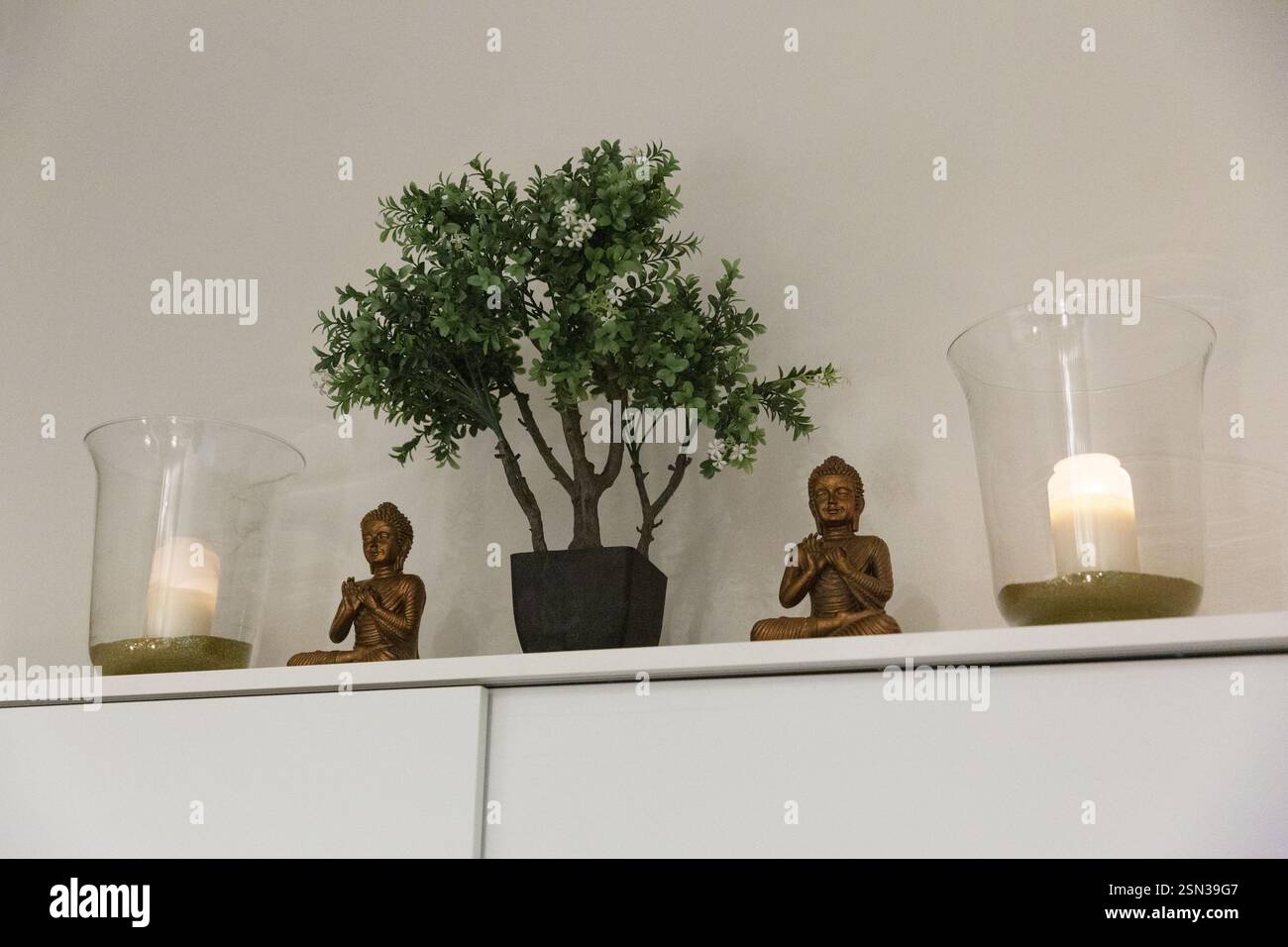 Statua del Buddha su una mensola bianca con candele e un albero. Foto Stock