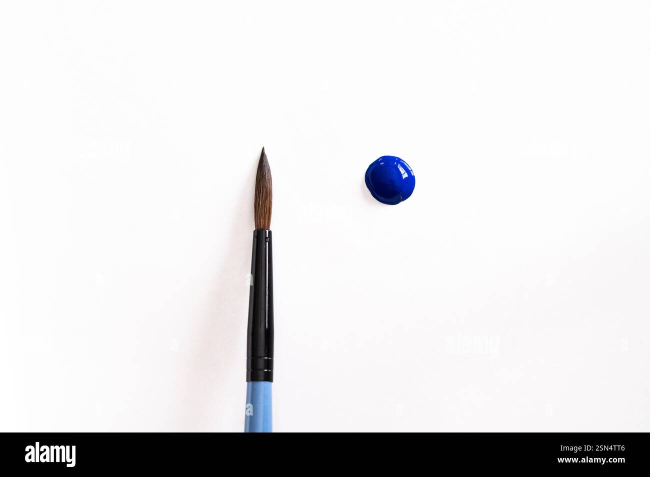 Una goccia di vernice blu accanto a un pennello pulito su sfondo bianco Foto Stock