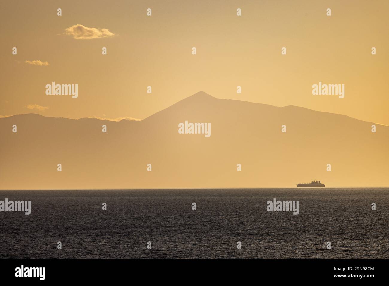 Una barca sta navigando su un mare calmo con una montagna sullo sfondo. Il cielo è un mix di tonalità arancio e blu, che creano un'atmosfera serena e tranquilla Foto Stock