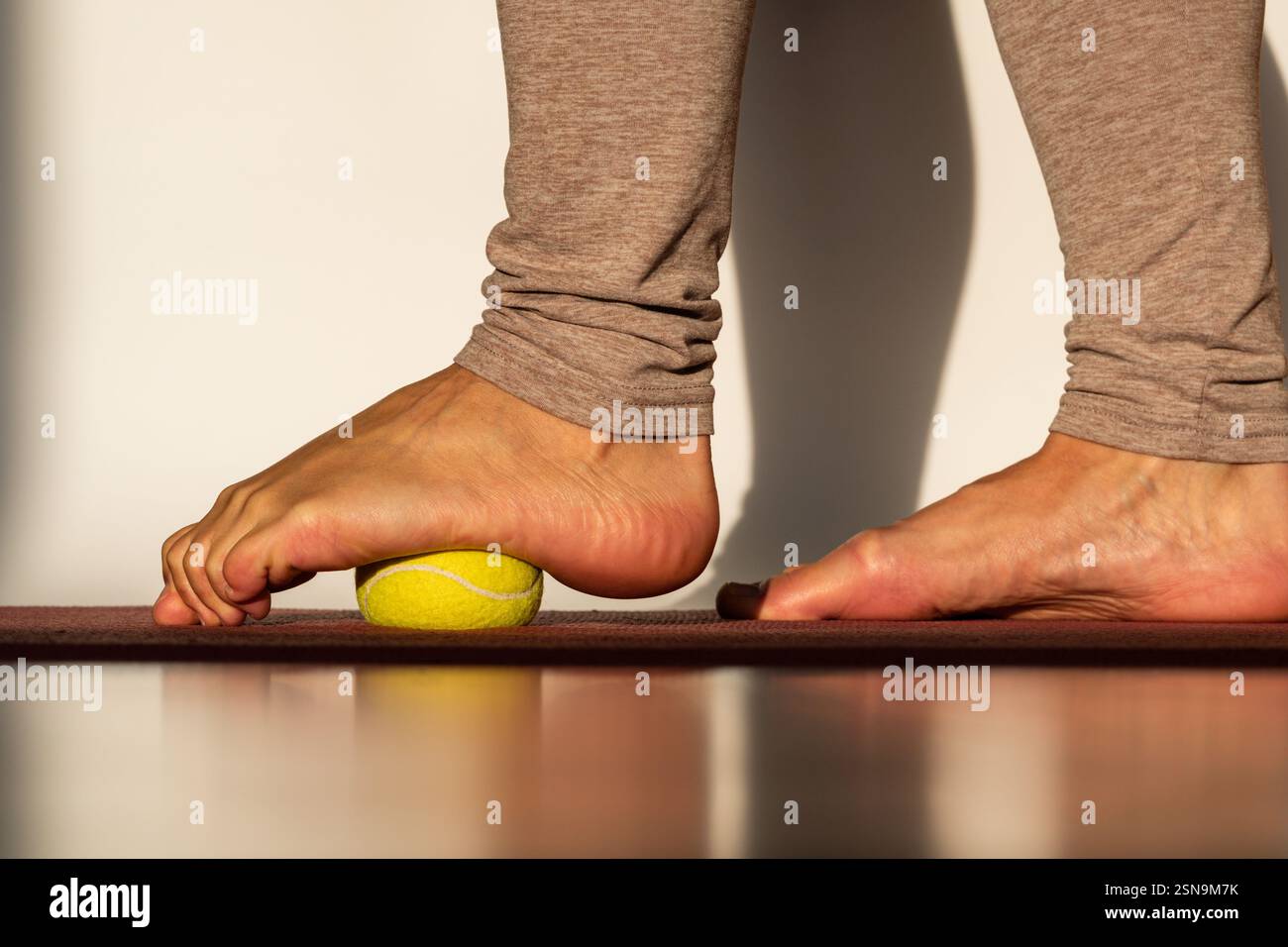 Rilassamento miofasciale dei muscoli del piede con una palla da tennis su un tappeto a casa, primo piano. Concetto sul tema della prevenzione del dolore ai piedi Foto Stock