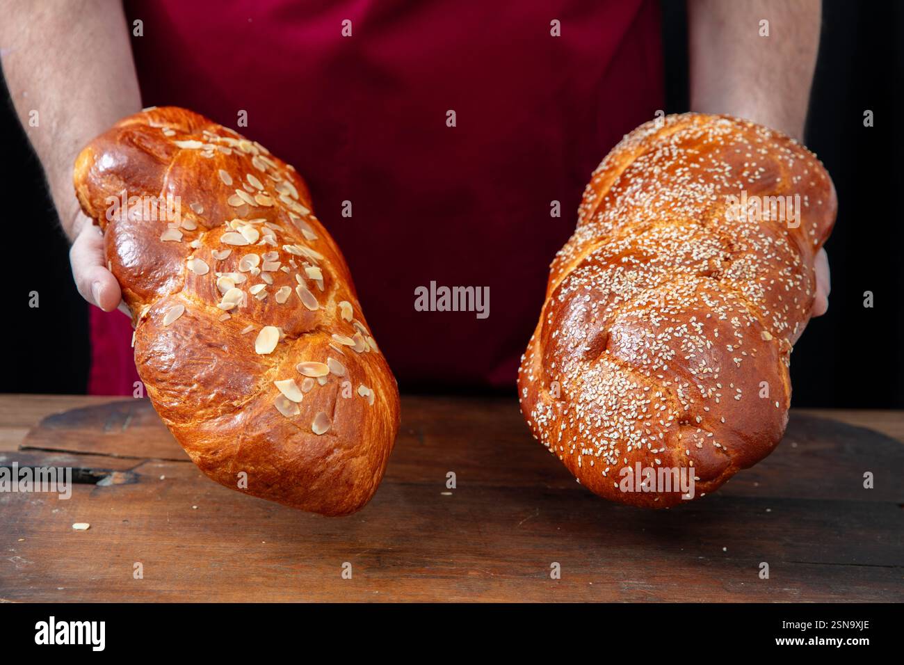 Pane dolce pasquale, mani di panettiere che tengono due tsoureki appena sfornate su un tavolo di legno, vista ravvicinata Foto Stock