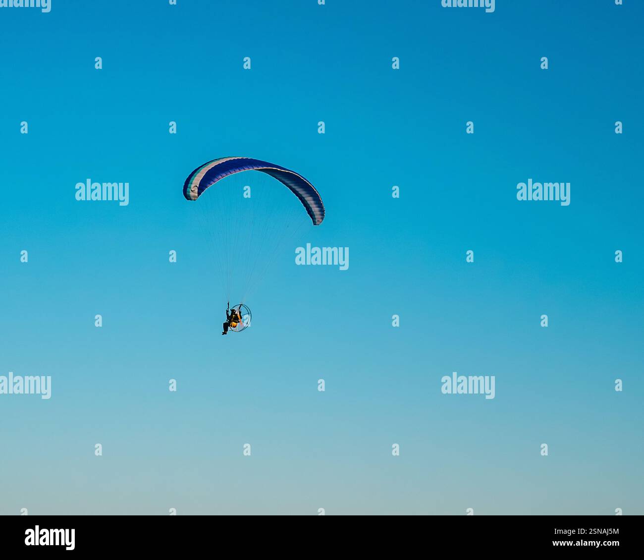 Pilota seduto alla guida di un parapendio motorizzato in un cielo azzurro e limpido Foto Stock