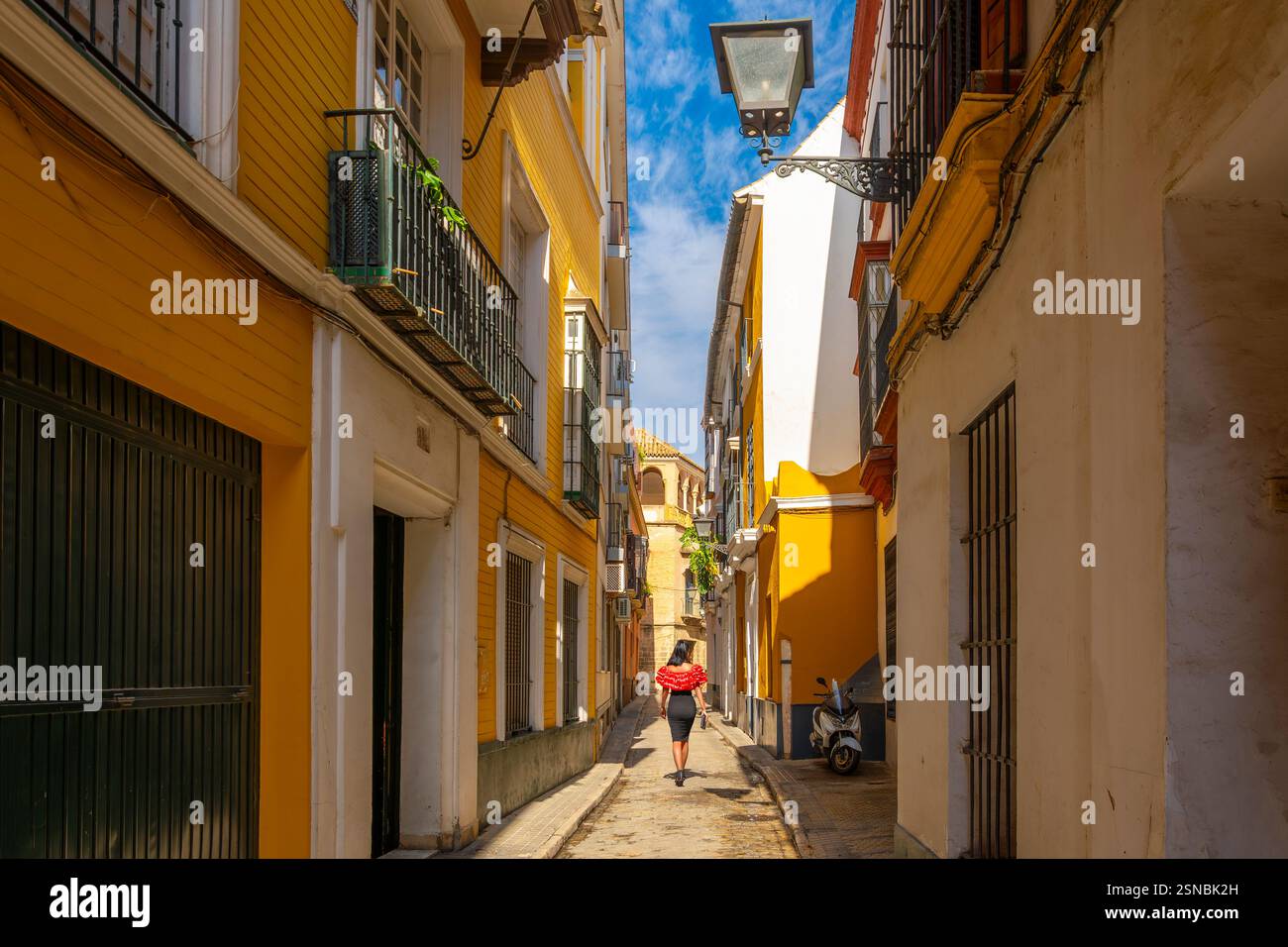 Una donna spagnola cammina lungo uno stretto vicolo nella colorata città vecchia di Barrio Santa Cruz nella città andalusa di Siviglia, Spagna. Foto Stock